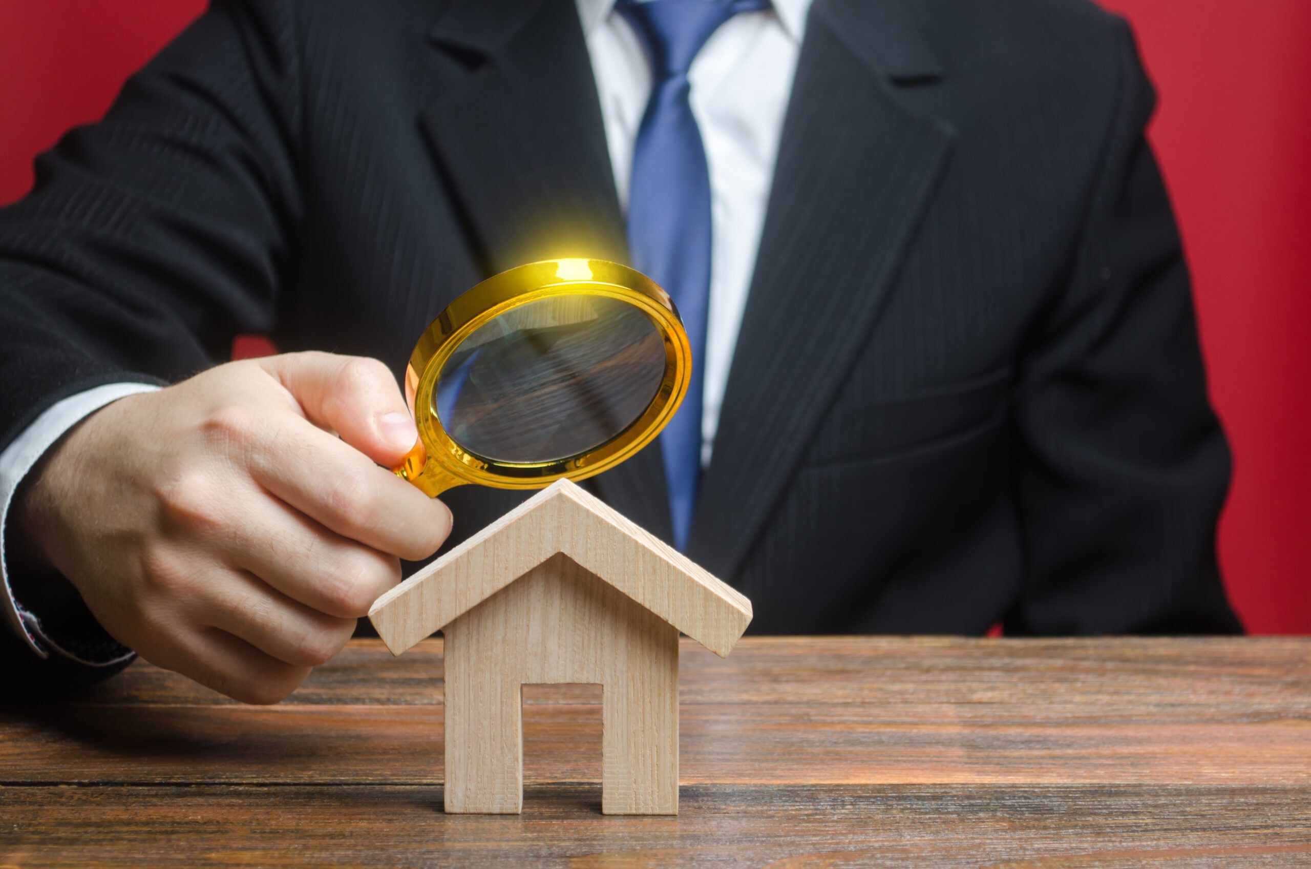Man Studying A miniature House model Through A Magnifying Glass.