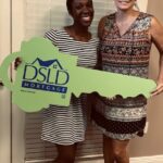 2 people posing for a photo holding a dsld sign