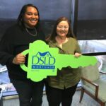 2 people posing for a photo holding a dsld sign