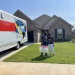 2 people posing in front of a sold house