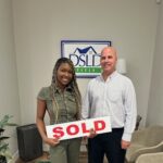 Two people holding a sold sign