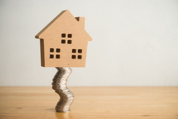 A wooden house on a stack of coins representing how to buy a foreclosure home